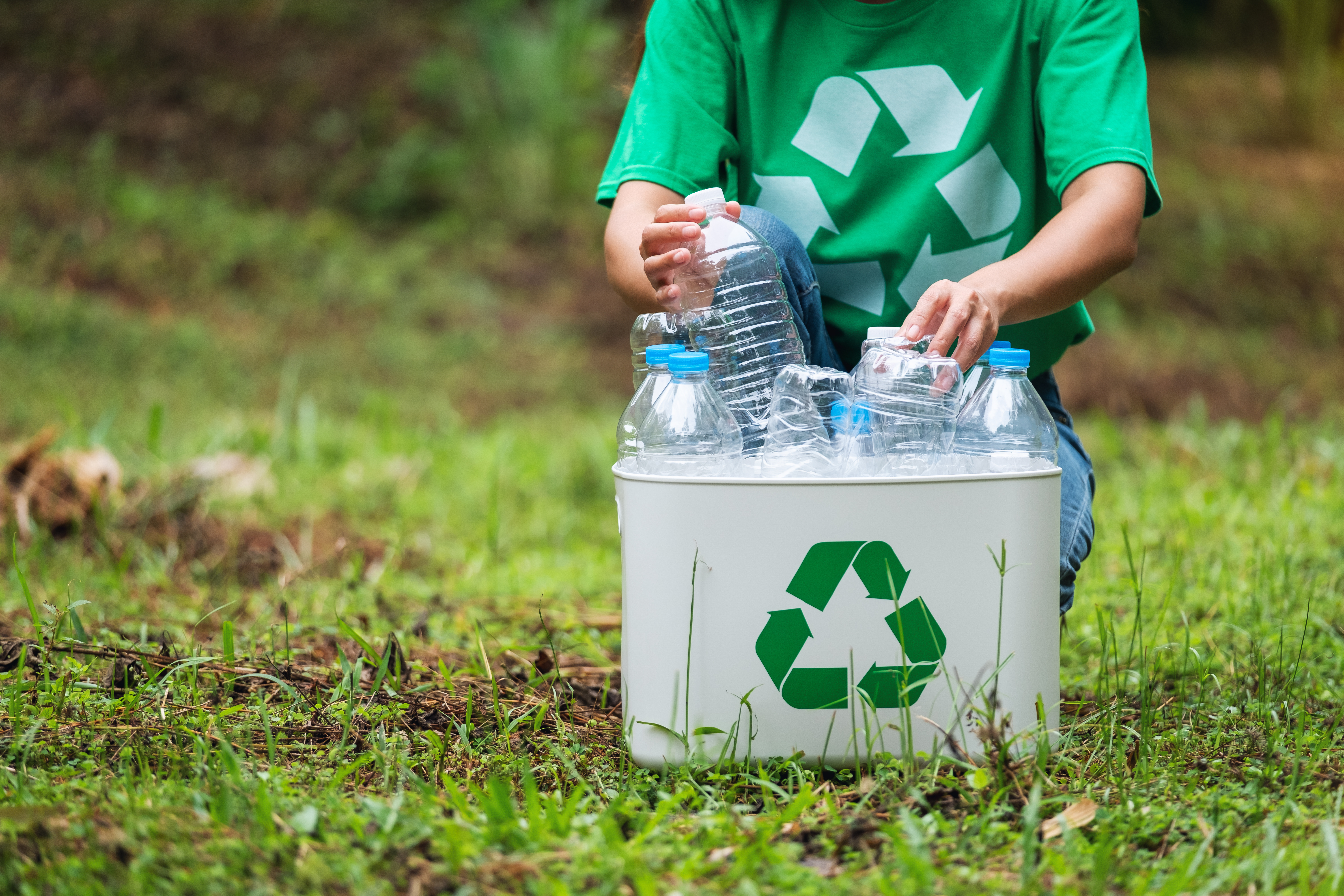 person in green shirt sorting touching holding plastic bottles in recycle bin